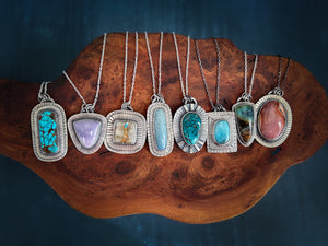8 gemstone necklaces of different colors on a curvy piece of wood. All handcrafted in my jewelry studio in Vermont