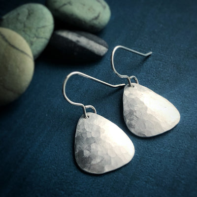 Little silver Grounded Earrings on blue background. Earrings are rounded triangles of hammered silver. Empowering jewelry, healing jewelry, handmade in VT