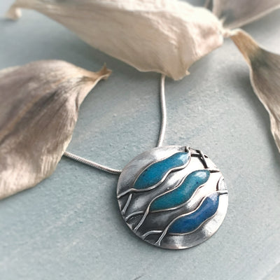 Finding Path Necklace silver domed circle with three currents of blue turquoise on grey background with white flower petals pendants with meaning empowering jewelry handmade in Vermont