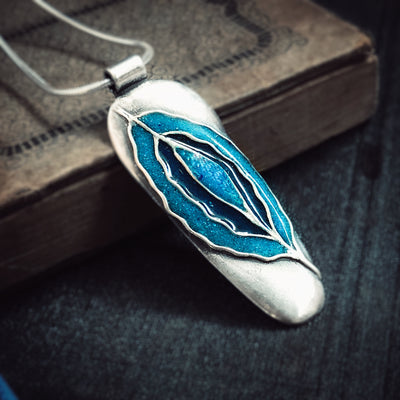 Inner Flow Necklace resting on antique book. Silver necklace with concentric blue waves made out of turquoise and lapis lazuli. Pendants with meaning, healing jewelry, empowering jewelry, handmade in Vermont.
