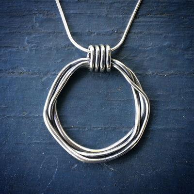 Silver Zen Coil Pendant on blue background. Necklace is silver strands coiled to make a circle. Empowering jewelry pendants with meaning. 