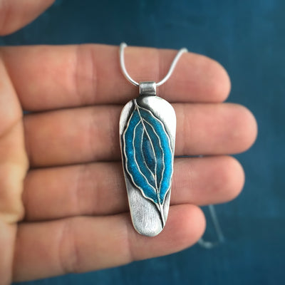 Hand holding Inner Flow Necklace. Silver with concentric blue waves made out of turquoise and lapis lazuli. Pendants with meaning, healing jewelry, empowering jewlery, handmade in Vermont.