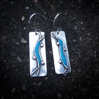 Silver Turquoise Creek Earrings on dark cement background. Earrings are Silver rectangles with a turquoise wave going down the middle, with three silver dots. Empowering jewelry Vermont. 