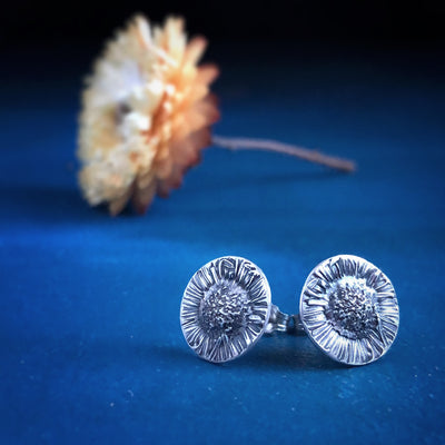 Silver Chamomile Stud Earrings on blue background with yellow flower in distance. Empowering healing jewelry handmade Vermont. 
