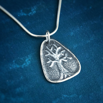Silver Triangle Tree of Life Necklace on blue background. Pendant is rounded triangle with raised relief of tree with branches. Pendants with meaning handcrafted Vermont. 
