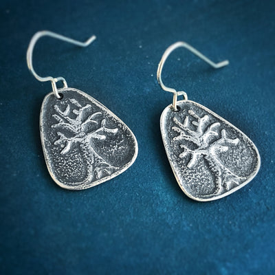 Silver Tree of Life Earrings. Two earrings that are rounded triangles with raised image of a tree with branches. On blue background. Handmade in Vermont. 