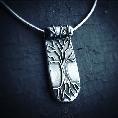 Silver Tree of Life Necklace on dark blue cracked background. Necklace has roots and branches that go over the bail. Pendants with meaning handmade Vermont. 